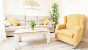 A living room with a beige sofa, a yellow armchair, a wooden coffee table, and a potted plant.