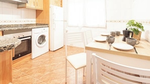 A kitchen with wooden cabinets, a washing machine, a stove, and a dining area with a table and chairs.