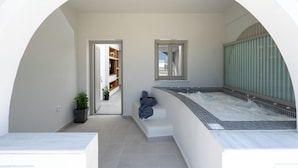 Een wellnessruimte met een jacuzzi, een zithoek en uitzicht op een tuin door een gebogen doorgang.