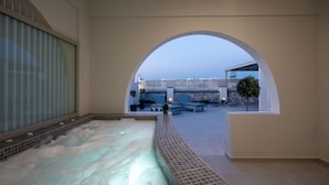 Een wellnessruimte met een bubbelbad, een stenen muur en uitzicht op zee.