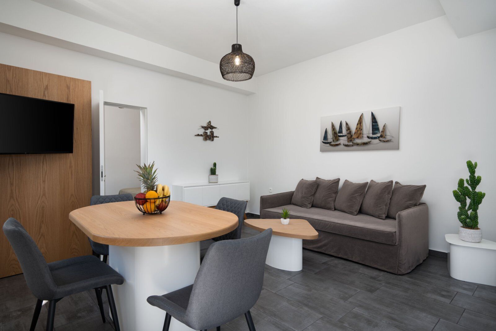 Ein modernes Wohnzimmer mit einem runden Holztisch, grauen Stühlen, einem grauen Sofa und einem kleinen weißen Beistelltisch.