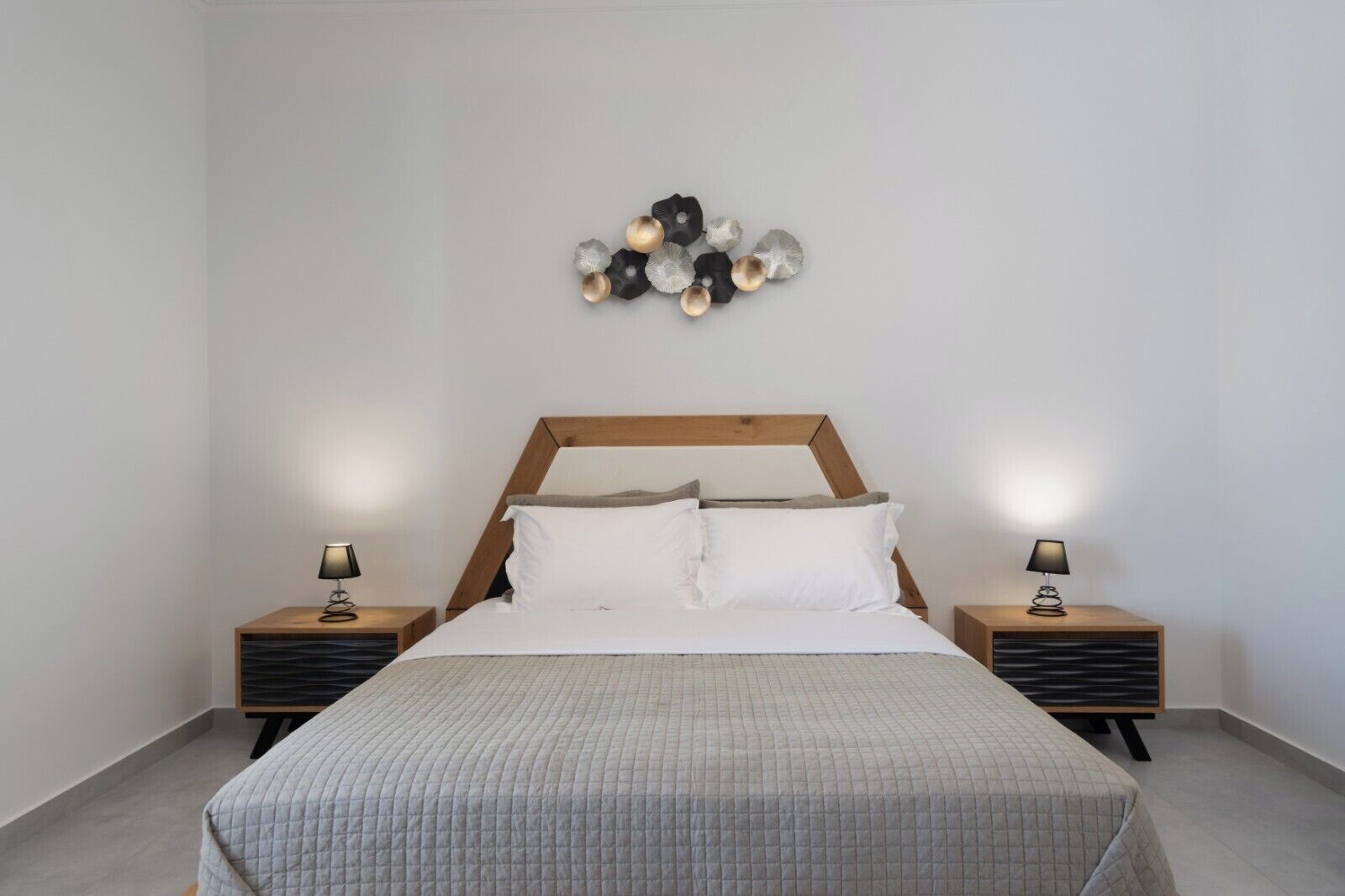 A bedroom with a bed, two bedside tables, and a wall-mounted light fixture.