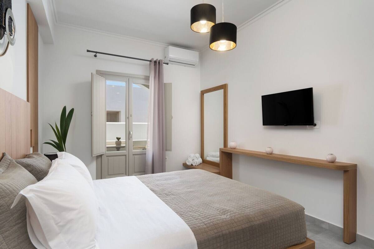Un dormitorio moderno con cama, mesita de noche, espejo y televisor montado en la pared.