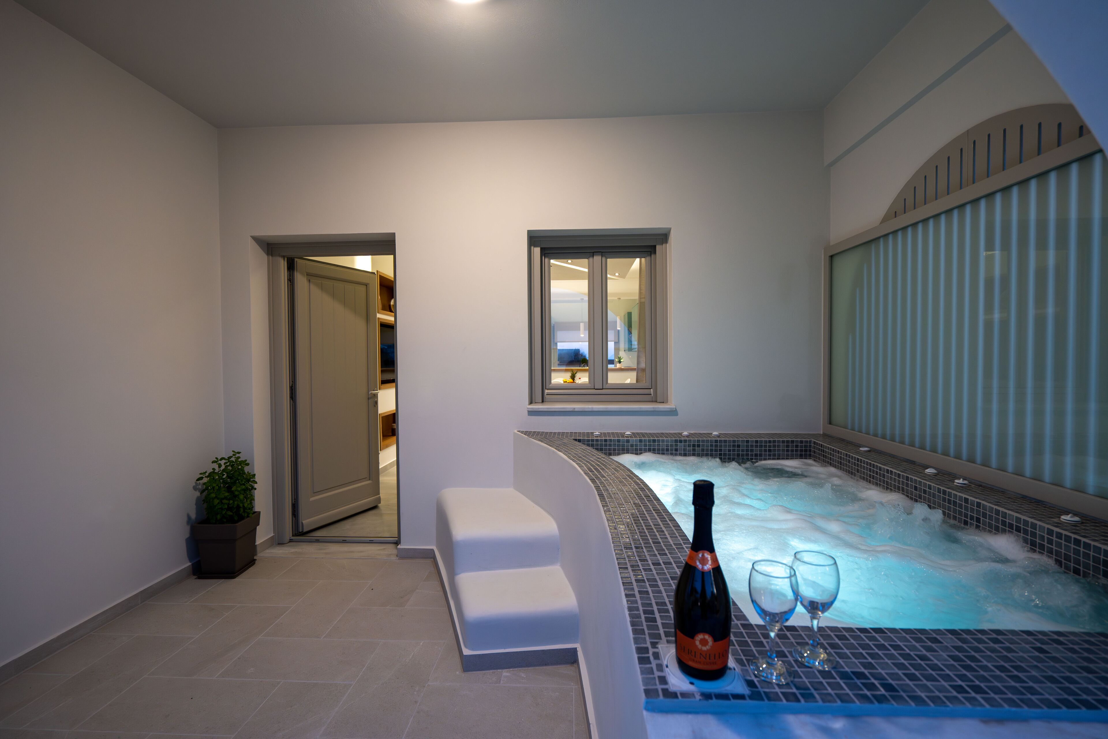 Zona de spa con un jacuzzi, una botella de vino y dos copas sobre una bandeja.