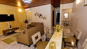 A modern living room with a sofa, armchairs, a glass coffee table, and a TV.
