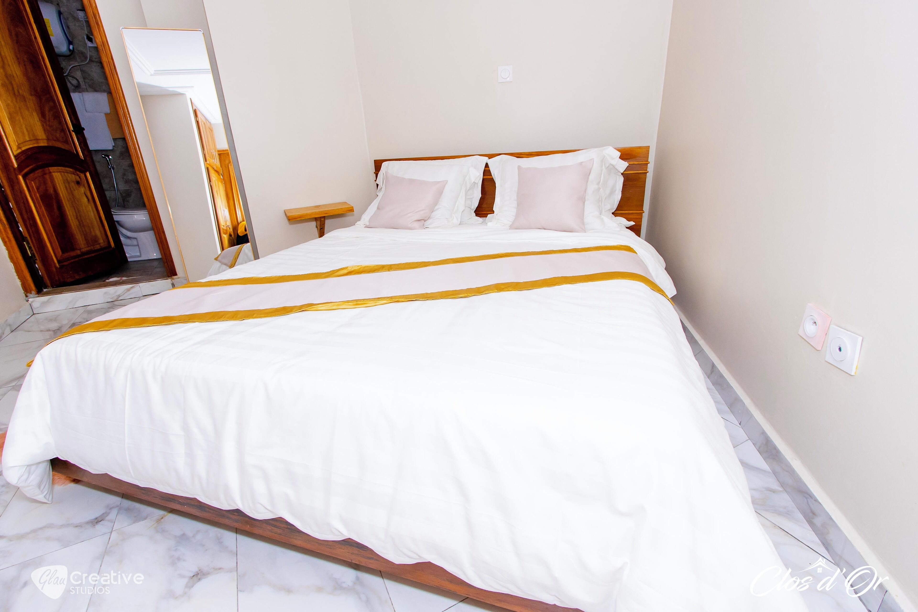 A neatly made bed with a white and yellow striped bedspread, a wooden headboard, and a small bedside table.