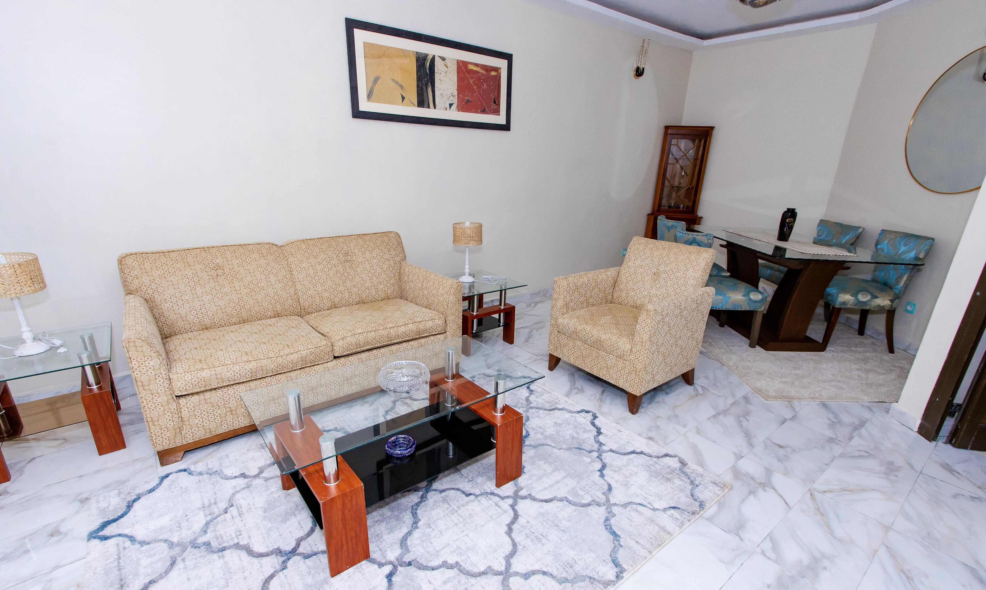 A living room with a sofa, armchair, glass coffee table, and a dining area with chairs and a table.