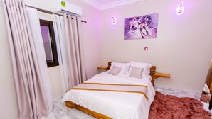 A bedroom with a bed, curtains, a painting, and an air conditioning unit.