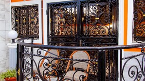 A balcony with ornate black wrought iron railings, a potted plant, and a ceiling fan.