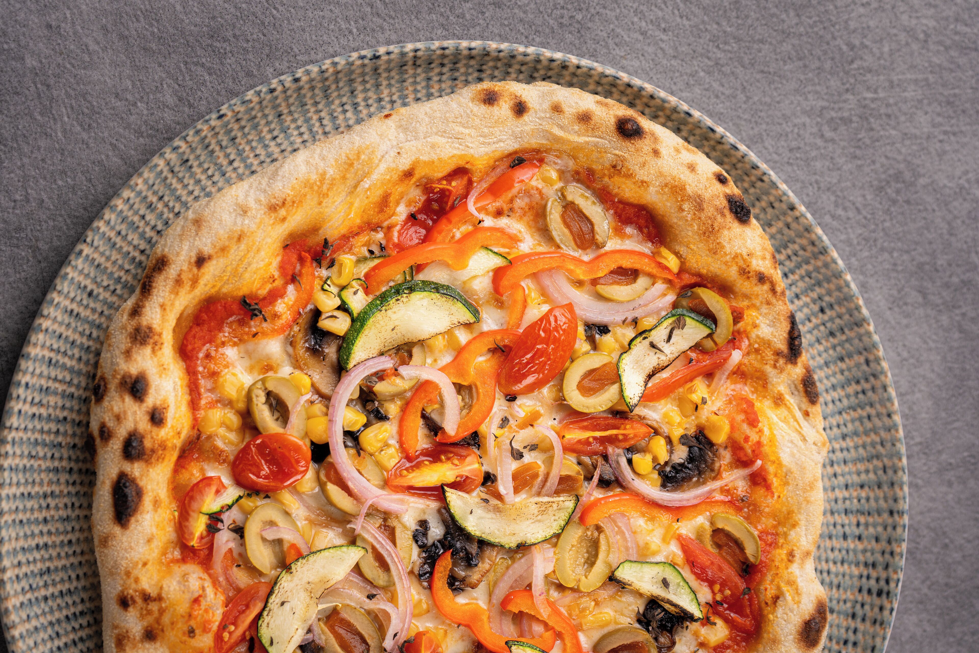Eine Pizza mit verschiedenen Gemüsesorten auf einem gewebten Teller.