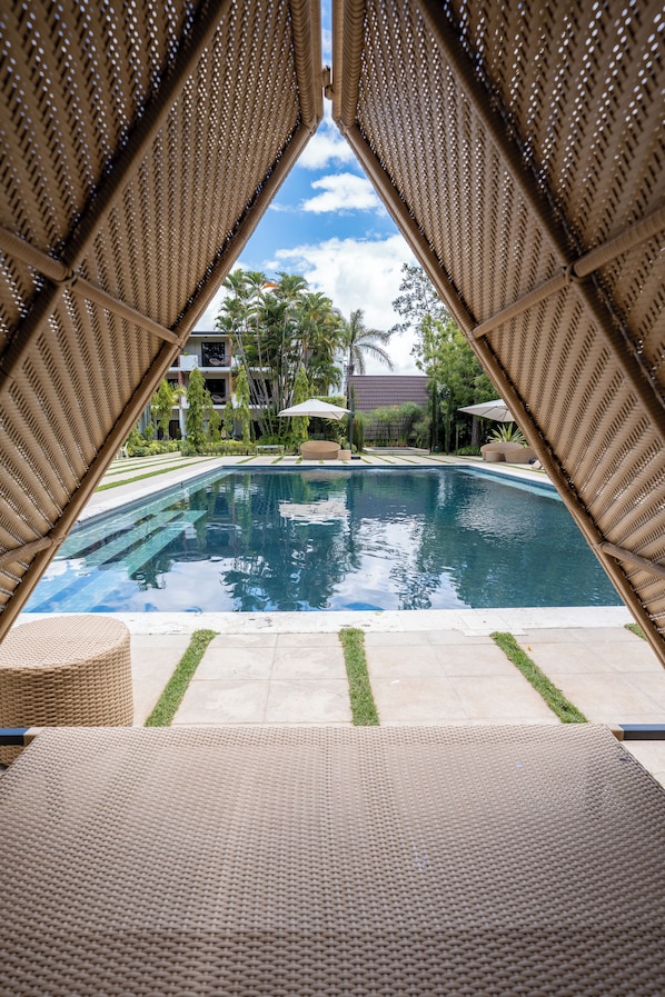 Zona de piscina con vista despejada, sillas de descanso y un edificio al fondo.