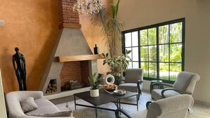 A modern living room with a fireplace, comfortable seating, and large windows offering a view of greenery. - Hotel Pinar Dorado by Gran Jimenoa (Jarabacoa)