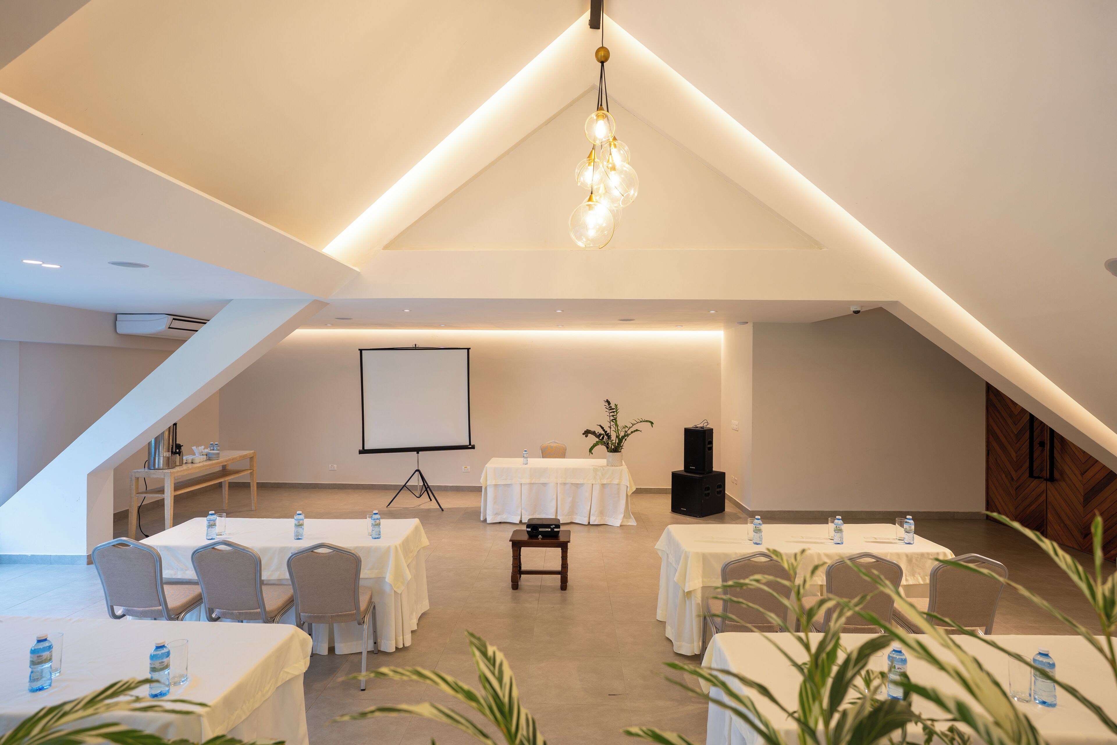 A conference room with tables, chairs, a projector screen, and a speaker.