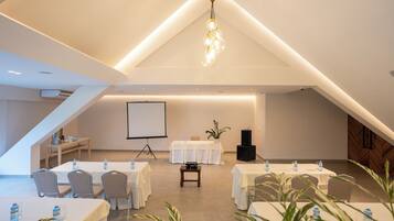 A conference room with tables, chairs, a projector screen, and a speaker.