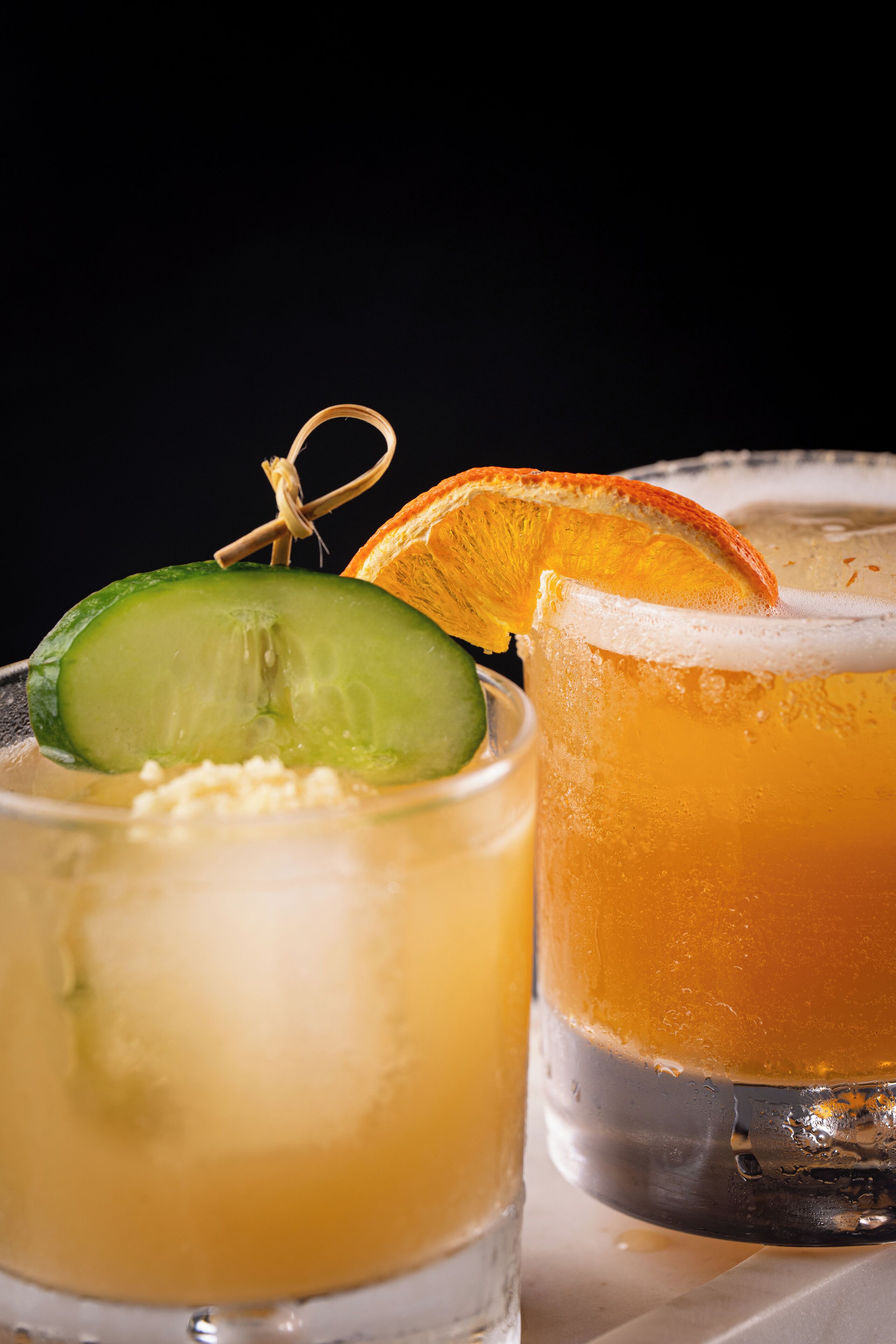 Two glasses of beverages, one with a lime slice and the other with an orange slice.