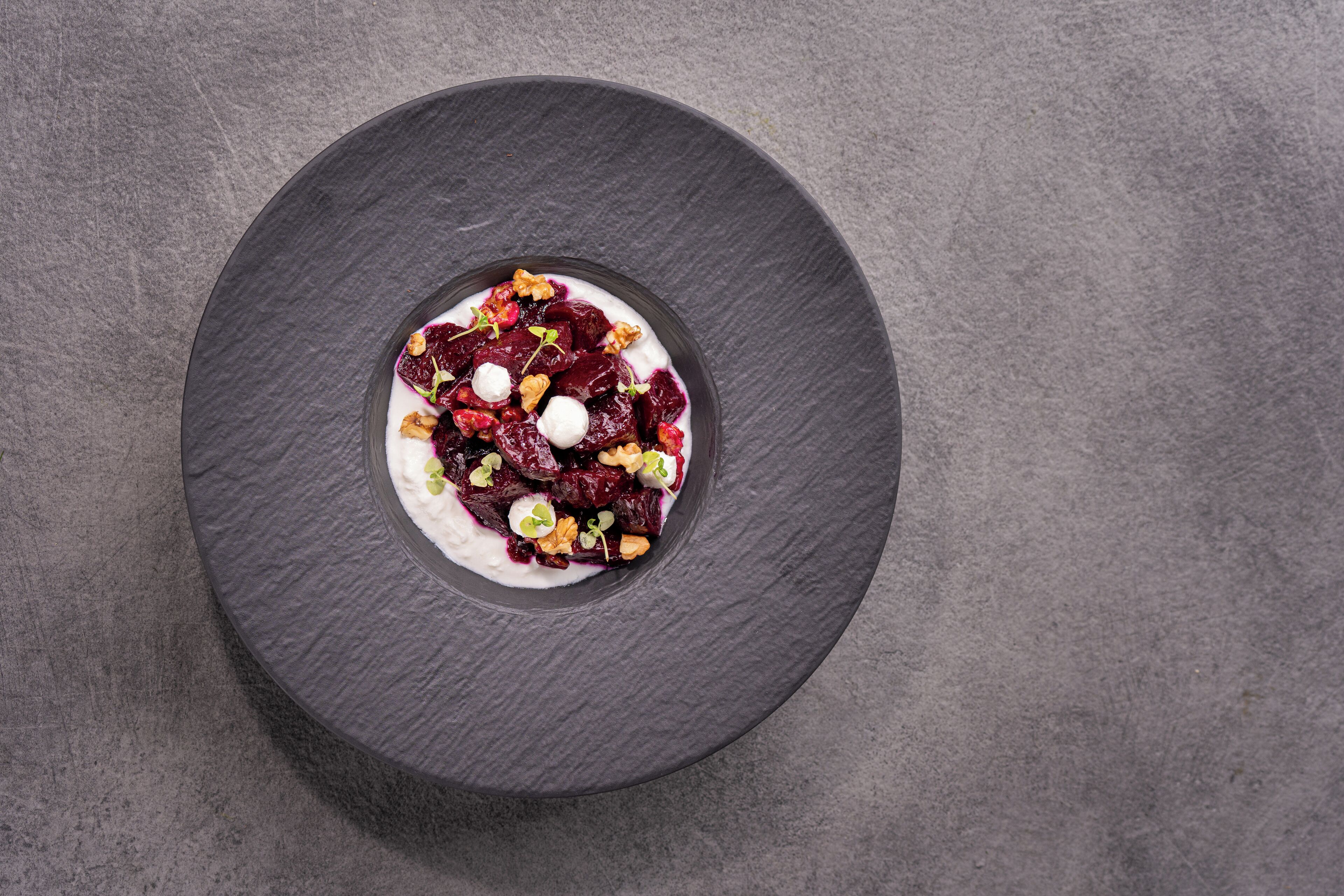 A round black slate plate with a dessert on a textured grey background.