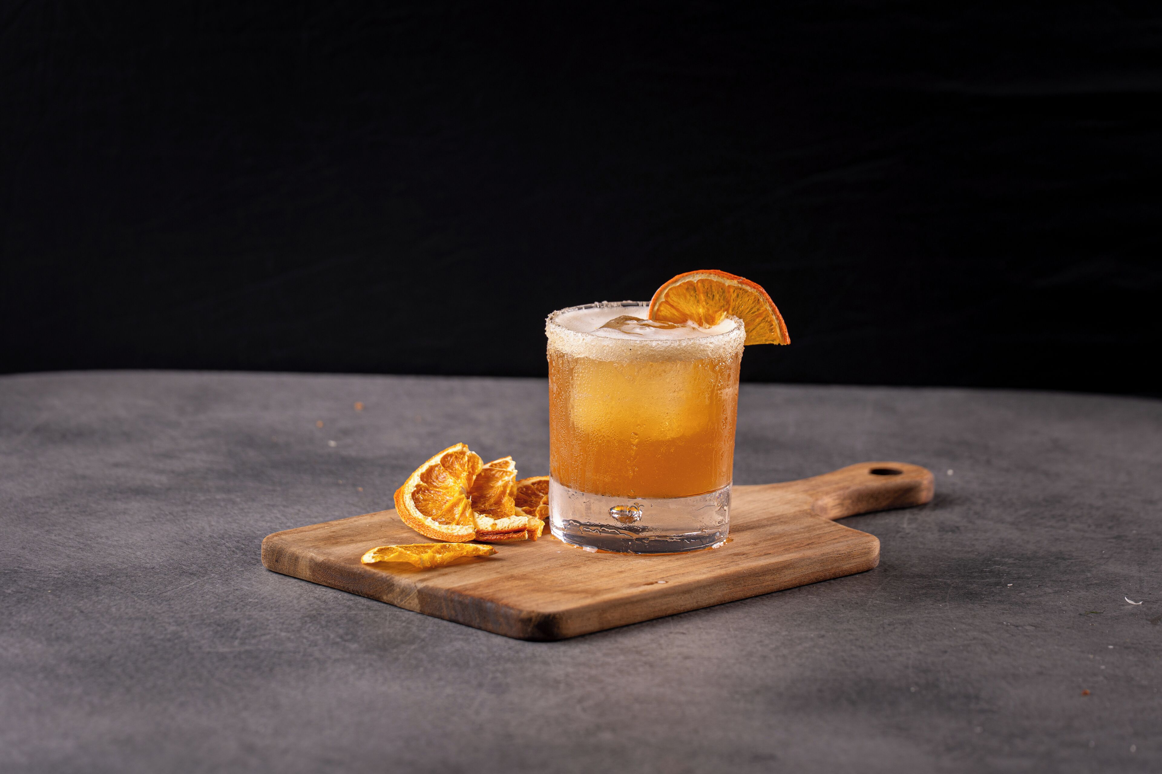 Un verre d’une boisson ambrée, posé sur une planche en bois, le tout sur un fond sombre.