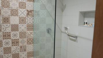 A bathroom with patterned tiles, a glass shower enclosure, a toilet, and a small shelf with toiletries.