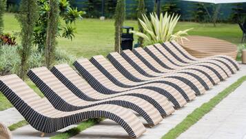 Una fila de sillones de descanso con un diseño tejido, dispuestos sobre un sendero pavimentado con bordes de césped.