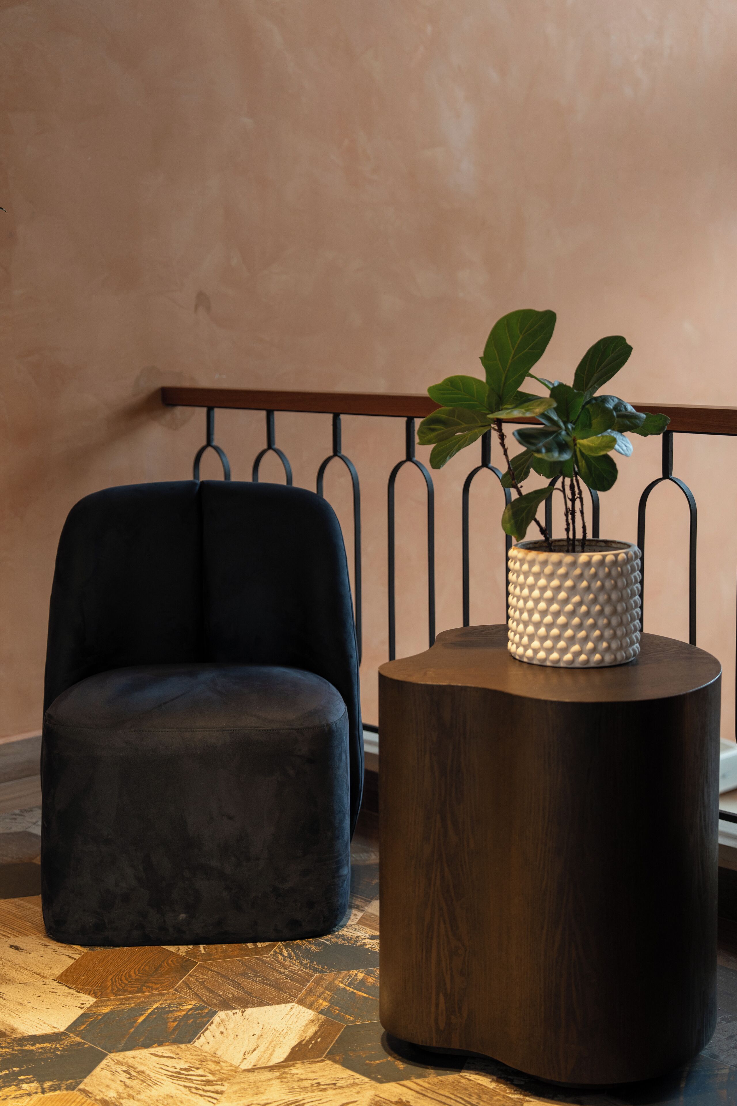A dark blue chair and a round wooden side table with a textured white pot containing a plant.