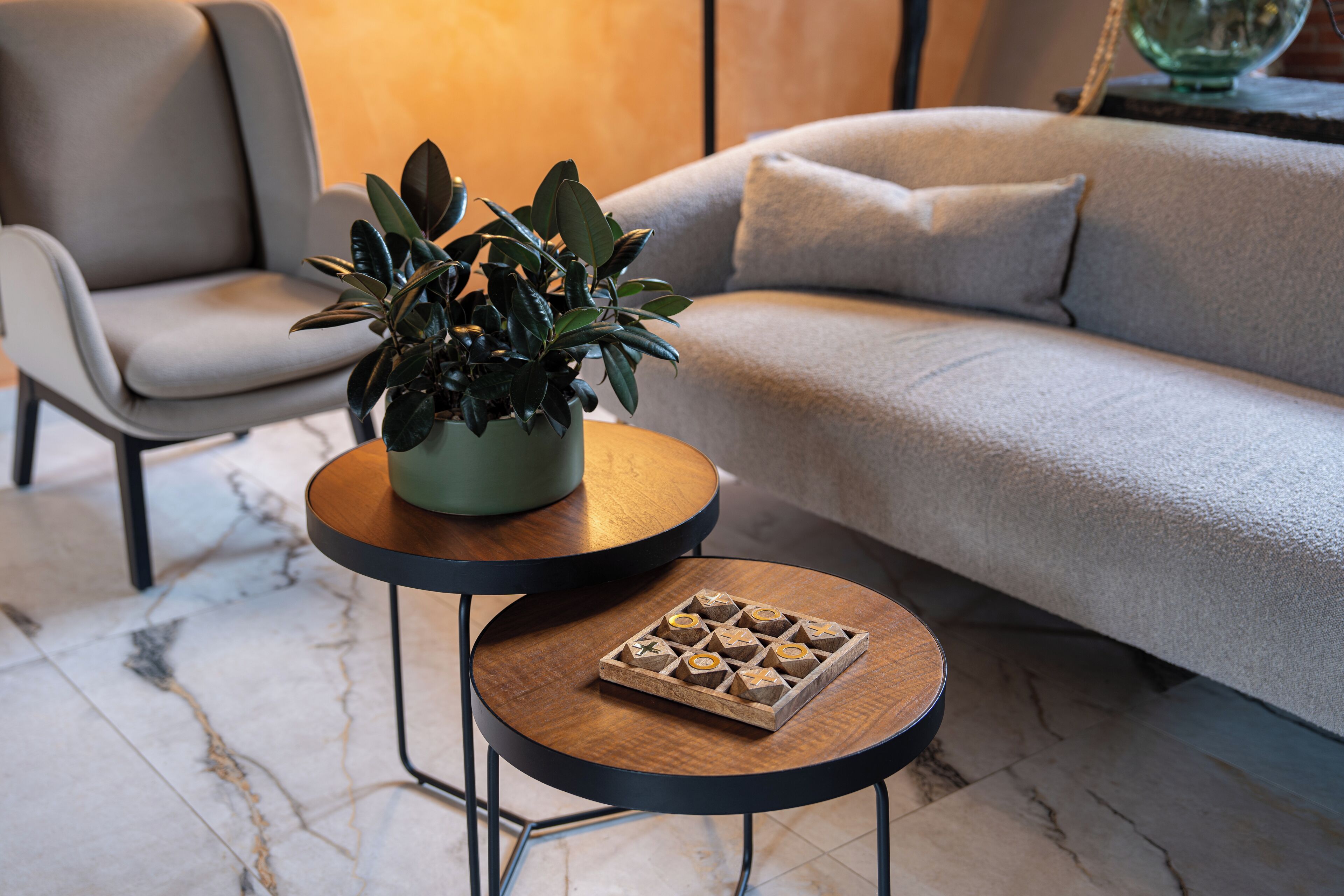 A modern living room with a grey sofa, a round wooden coffee table with a plant and a tray of chocolates, and a grey armchair.