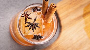 A glass with a beverage garnished with star anise and cinnamon sticks.