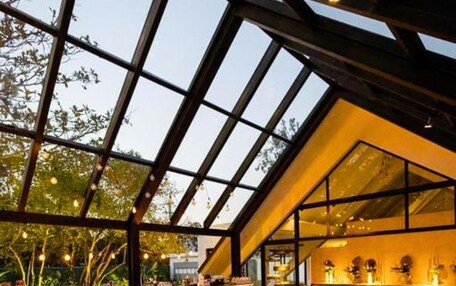 An indoor dining area with a high ceiling and large windows, featuring a modern design with wooden accents and black chairs.