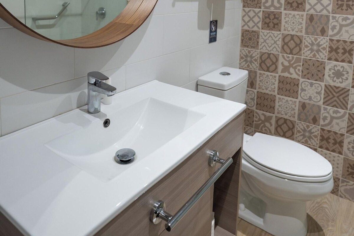 A bathroom with a white sink, a mirror, a toilet, and patterned tiles on the wall.