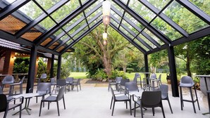 An outdoor patio with a glass roof, surrounded by chairs and tables, and a view of a garden with trees and plants. - Hotel Pinar Dorado by Gran Jimenoa (Jarabacoa)