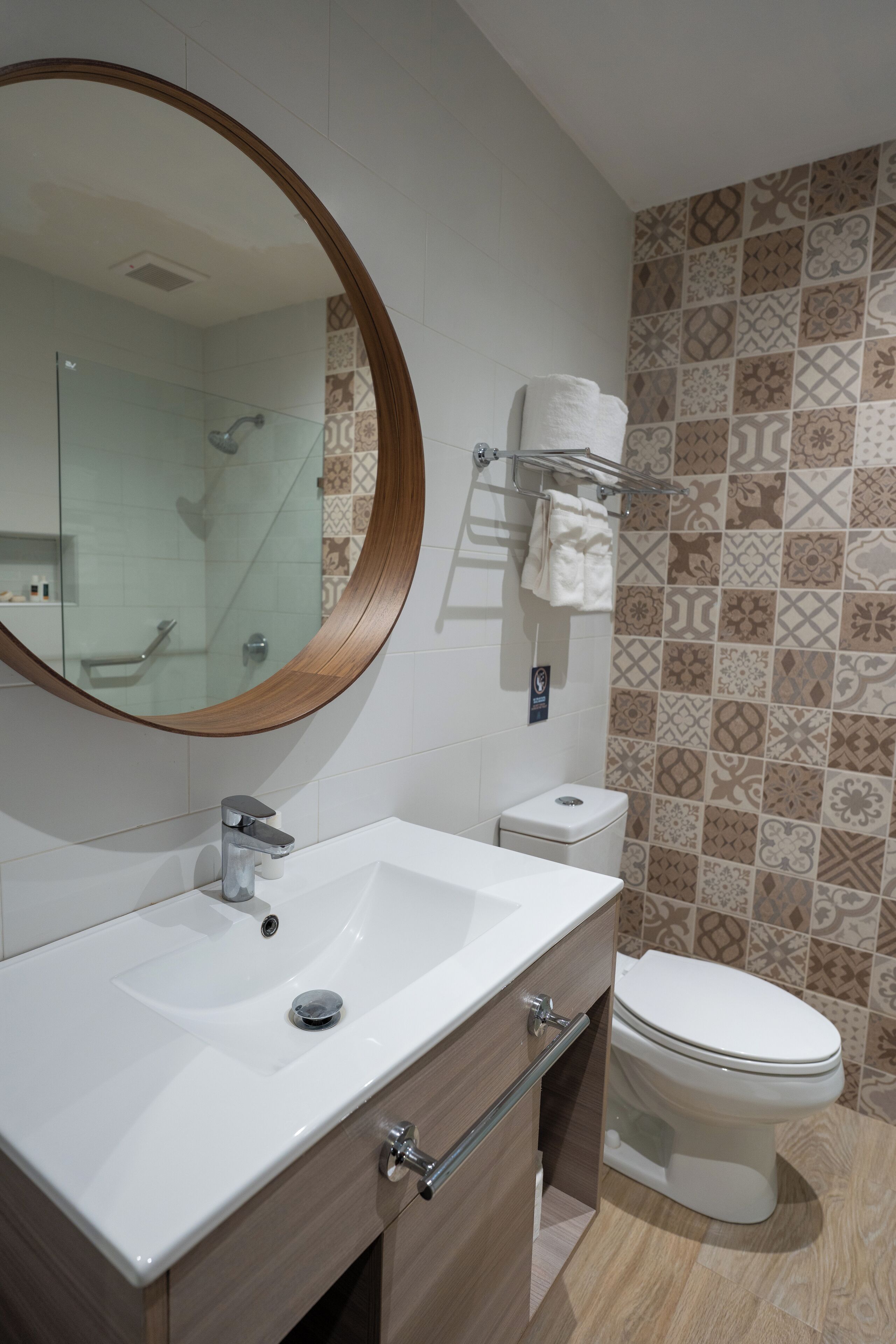 Une salle de bain avec un lavabo blanc, un miroir, des toilettes et des carreaux décoratifs sur le mur.