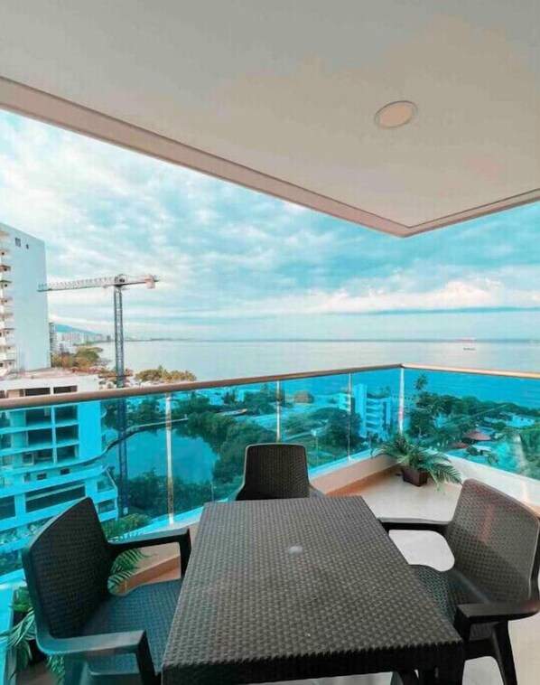 A balcony with a table and chairs, overlooking a body of water and a construction site.