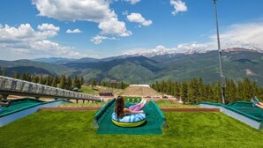 A person sitting on a green inflatable tube in a grassy area with a scenic mountain view. - Vail Sonnenalp King Hotel Room (Vail)