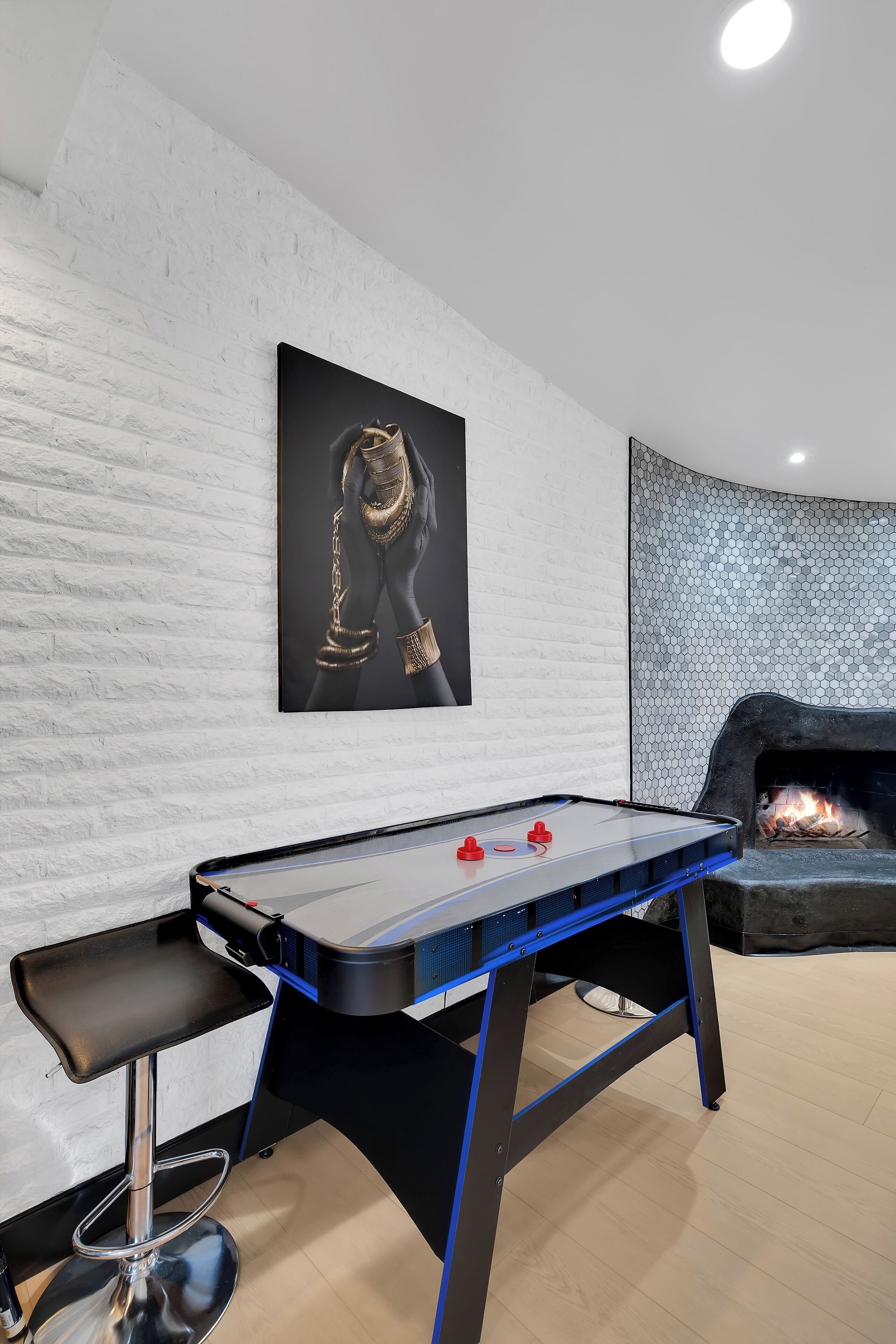 Un tavolo da calcio con decorazioni nere e blu, uno sgabello da bar e un camino con un muro alle spalle caratterizzato da un motivo esagonale.