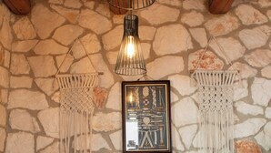 Comedor con pared de piedra, techo de madera, adornos de macramé, un cuadro enmarcado y una mesa lista para cuatro.