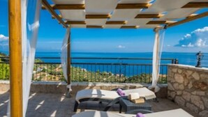 Una zona de estar al aire libre cubierta, con un muro de piedra y vistas al mar.