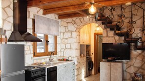 A kitchen with a stone wall, wooden beams, a built-in stove, a dishwasher, and a television. - Socrates Three Bedroom Villa With Sea View (Xirokastello)