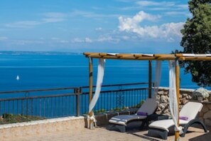 Eine Strandterrasse mit einer Pergola, Liegestühlen und Blick auf den Ozean.
