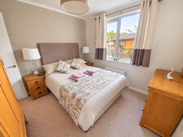 Une chambre à coucher comprenant un lit, des tables de chevet, un radiateur, une fenêtre avec des rideaux et une armoire en bois.