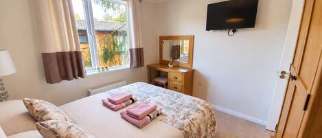 A bedroom with a bed, a dresser, a mirror, a TV, and a window with curtains.