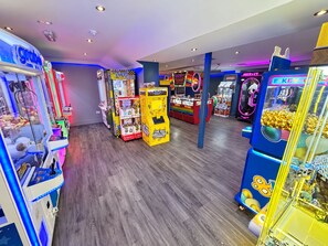 A row of claw machines with various prizes, a vending machine labeled 'The Big Yellow Change,' and a neon sign reading 'SNIP-IT.'