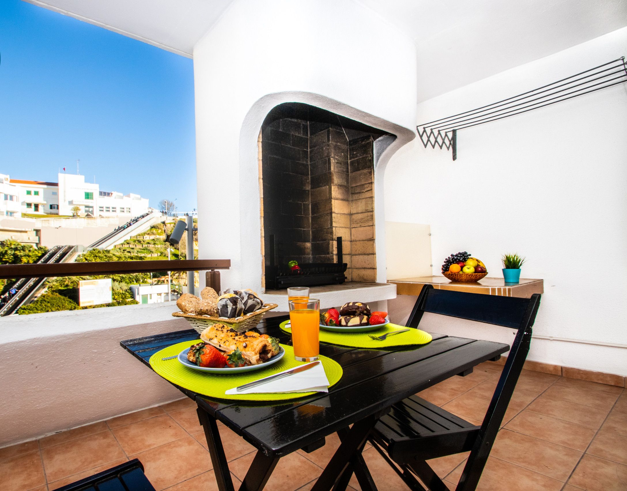 Un balcon avec une table dressée pour deux personnes, où l’on peut déguster un repas composé de pain, de fruits et d’un verre de jus d’orange.
