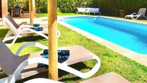 Zona de piscina amb gandules, una sobrera de palla i un cel blau clar.