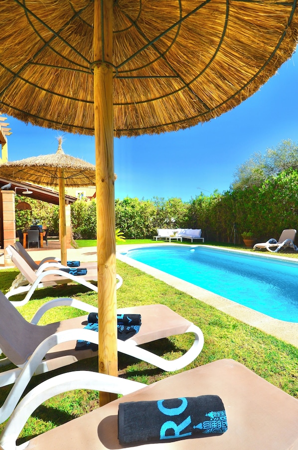 A poolside area with lounge chairs, a thatched umbrella, and a clear blue sky.