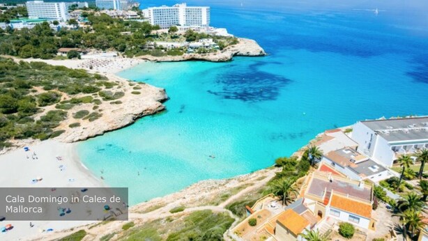 Cala Domingo a Cales de Mallorca, amb una platja, aigües turqueses cristal·lines i edificis als voltants.