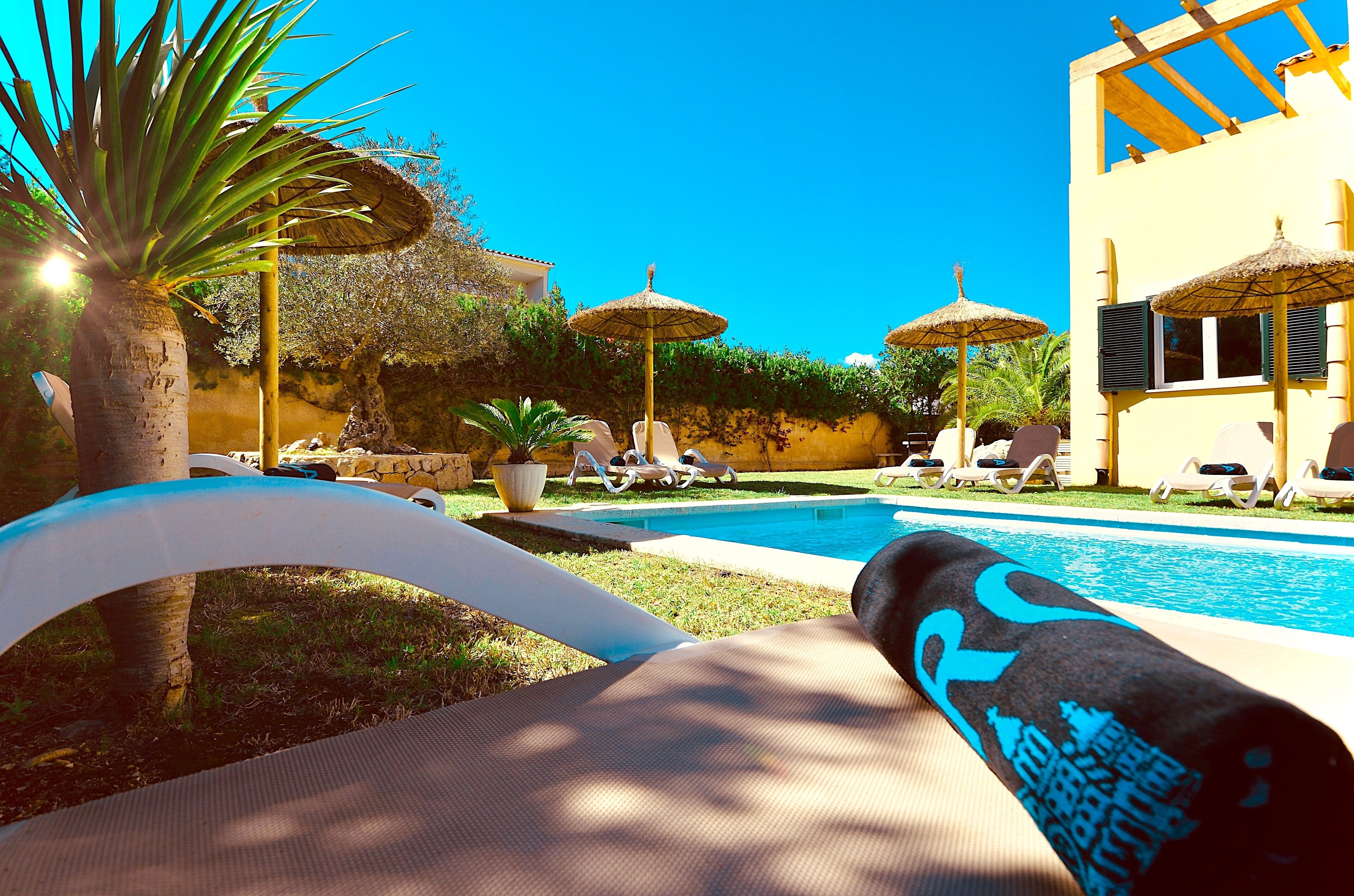 Un espace aménagé au bord de la piscine, avec des chaises longues, des parasols et un ciel d’un bleu limpide.