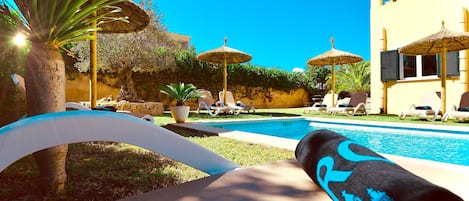Un espace aménagé au bord de la piscine, avec des chaises longues, des parasols et un ciel d’un bleu limpide.