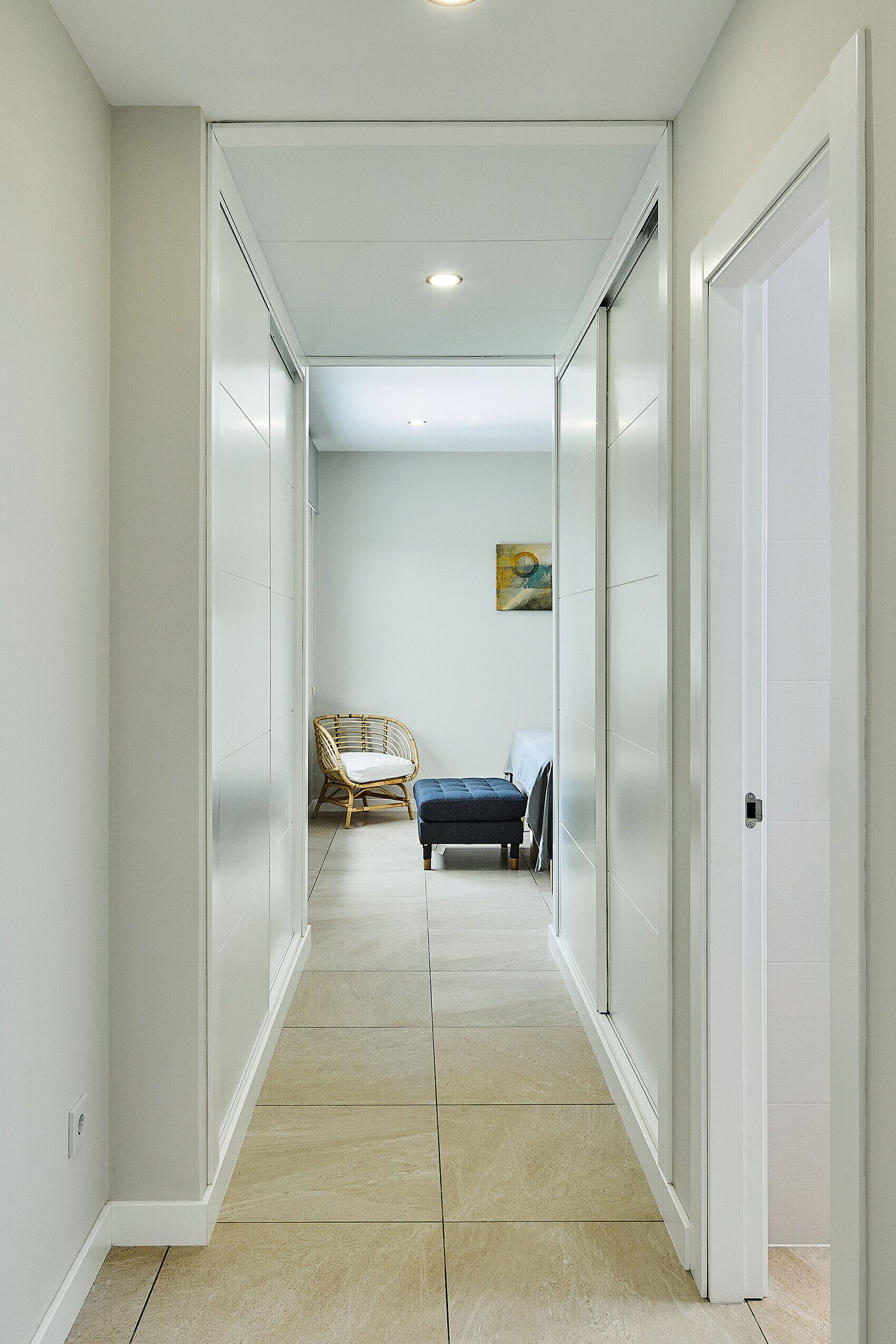 Un couloir avec un fauteuil en rotin, un banc et un tableau accroché au mur.