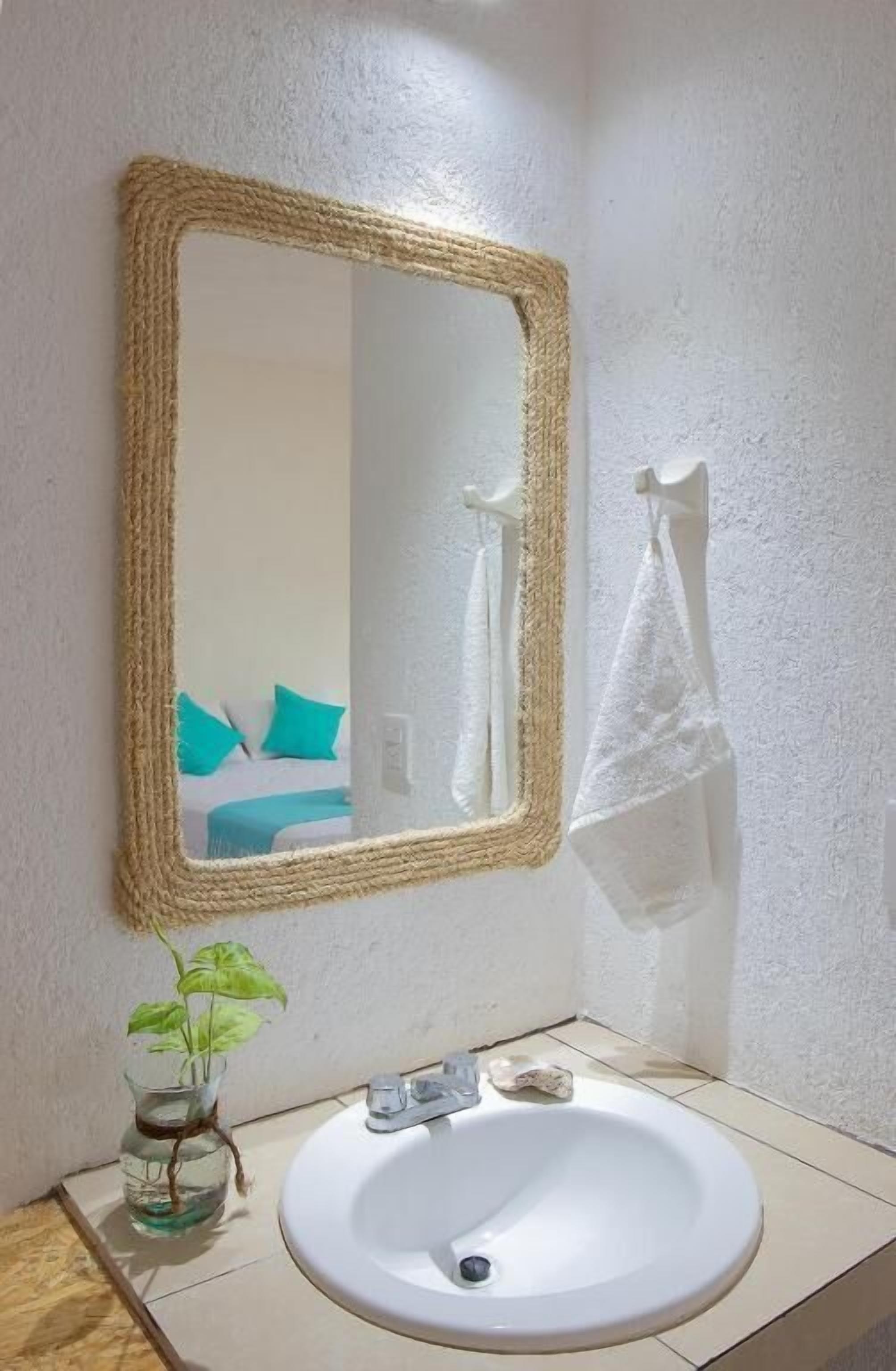 Uma casa de banho com uma pia branca, um espelho com moldura trançada e uma toalha pendurada num gancho.