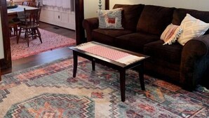 A cozy living room with a brown sofa, a patterned rug, and a dining area with a table and chairs. - Boho Bungalow off Main-one block from Lovely Park (Richmond)