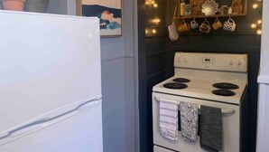 A kitchen with a white refrigerator, a white stove, and a wall-mounted shelf with kitchen utensils and a framed picture. - Boho Bungalow off Main-one block from Lovely Park (Richmond)